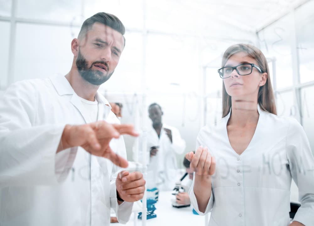 Young scientists man and woman stand by transparent wall with formulas